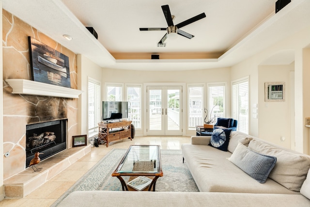 tiled living room with french doors, ceiling fan, a raised ceiling, and a fireplace