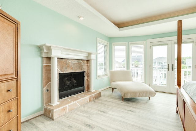 living room with light hardwood / wood-style floors, a stone fireplace, and a tray ceiling