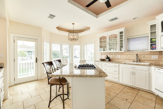 kitchen featuring a tray ceiling, white cabinetry, sink, pendant lighting, and a center island