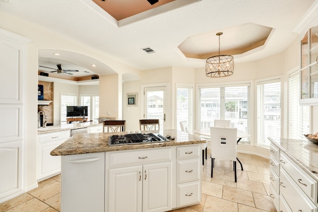 kitchen featuring stainless steel gas stovetop, ceiling fan, a healthy amount of sunlight, and a tray ceiling