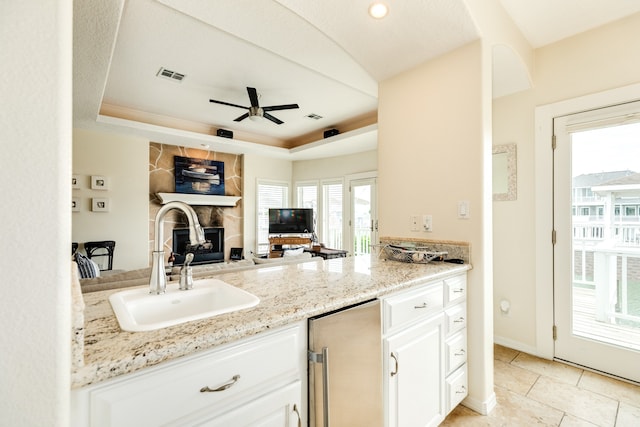 kitchen with white cabinets, sink, a tray ceiling, and a large fireplace