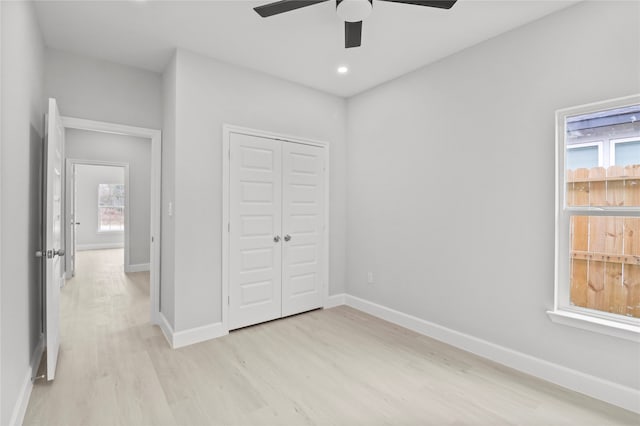 unfurnished bedroom featuring a closet, multiple windows, ceiling fan, and light wood-type flooring