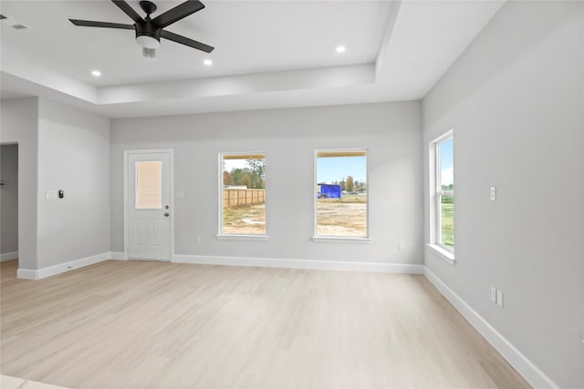 unfurnished room featuring light hardwood / wood-style floors, ceiling fan, and a tray ceiling