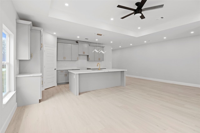 kitchen featuring tasteful backsplash, light wood-type flooring, gray cabinets, hanging light fixtures, and a kitchen island with sink