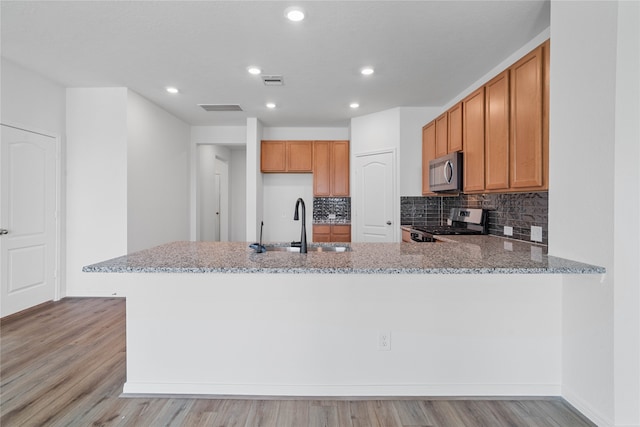 kitchen with kitchen peninsula, appliances with stainless steel finishes, light stone counters, and light hardwood / wood-style flooring