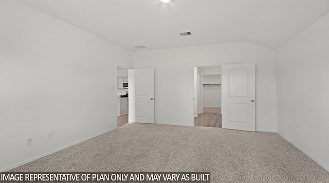 unfurnished bedroom with a spacious closet, light carpet, and vaulted ceiling