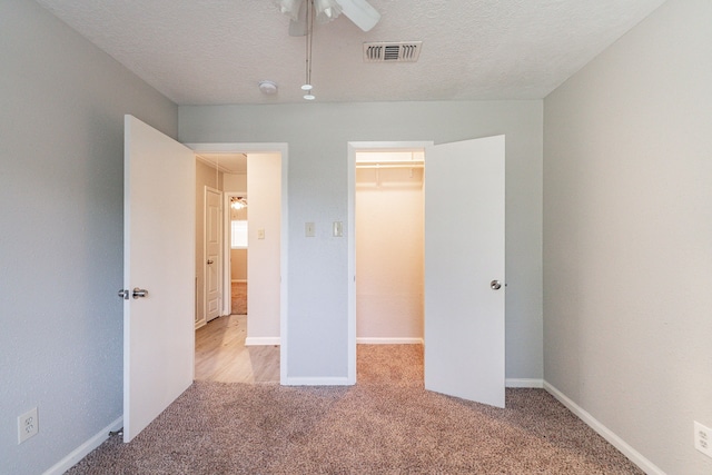 unfurnished bedroom featuring light colored carpet, ceiling fan, a textured ceiling, a closet, and a walk in closet