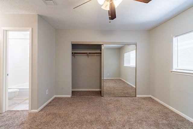 unfurnished bedroom with ceiling fan, a textured ceiling, a closet, carpet, and connected bathroom