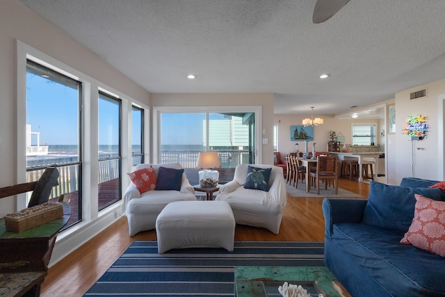 living room with wood-type flooring, a water view, a notable chandelier, and a textured ceiling