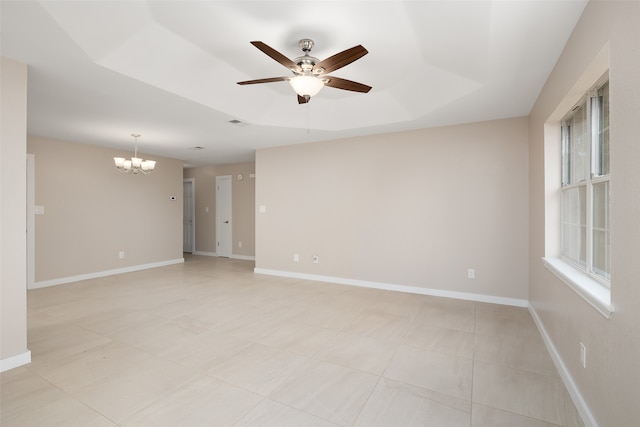 spare room featuring a raised ceiling, plenty of natural light, and ceiling fan with notable chandelier