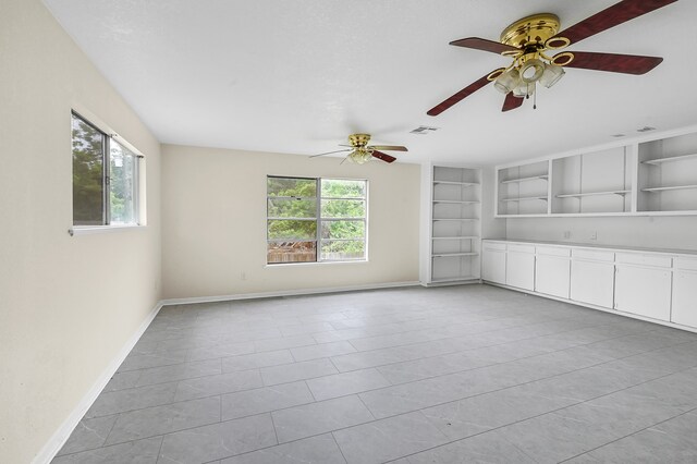 tiled empty room with plenty of natural light, ceiling fan, and built in shelves