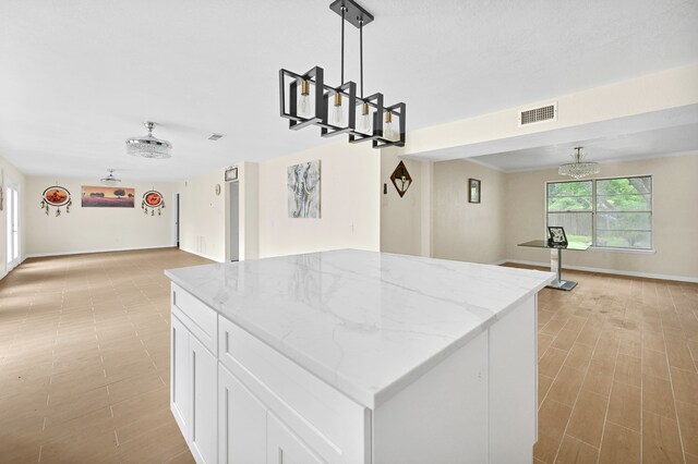 kitchen featuring light stone countertops, pendant lighting, a center island, and white cabinetry