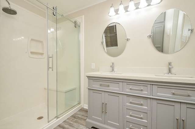 bathroom featuring a shower with door, hardwood / wood-style flooring, dual vanity, and ornamental molding