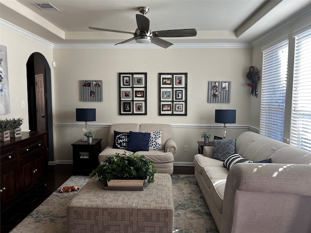 living room featuring ceiling fan, a tray ceiling, dark wood-type flooring, and ornamental molding