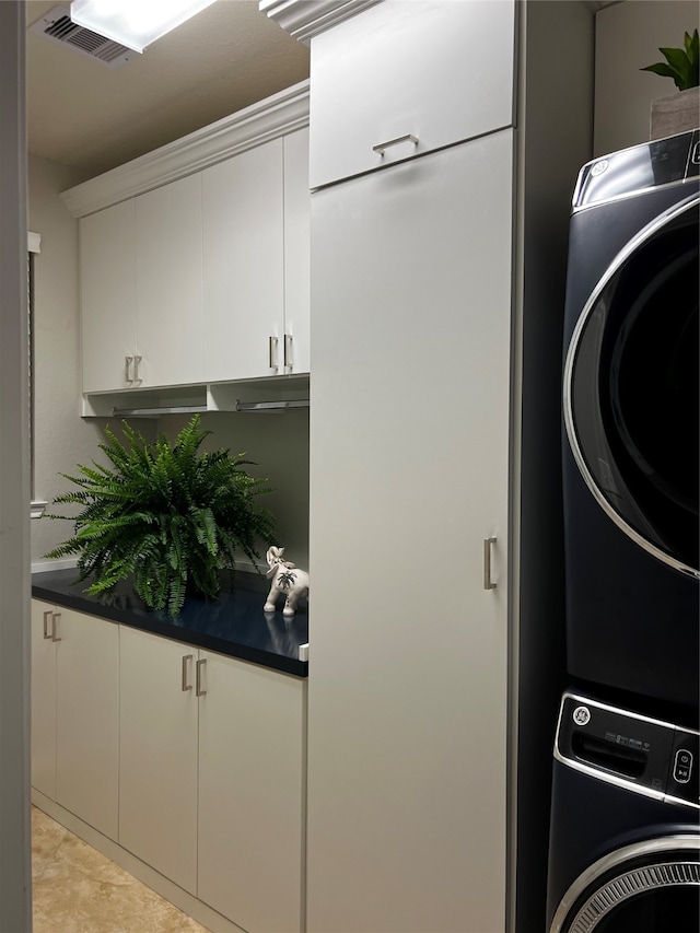 laundry area featuring stacked washing maching and dryer, cabinets, and light tile flooring