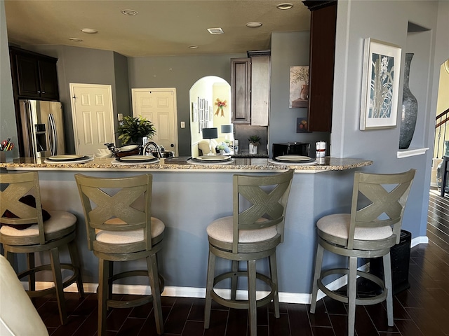 kitchen with stainless steel fridge with ice dispenser, kitchen peninsula, a kitchen bar, and light stone countertops