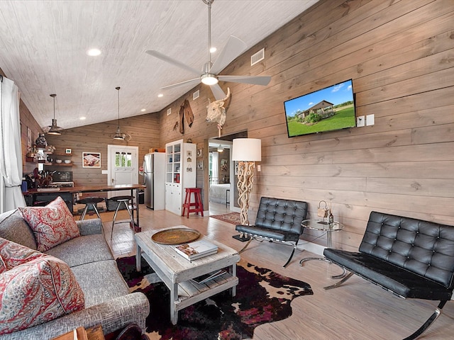 living room with high vaulted ceiling, light hardwood / wood-style floors, ceiling fan, and wood walls