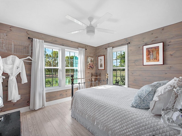 bedroom with wood walls, ceiling fan, and light hardwood / wood-style flooring