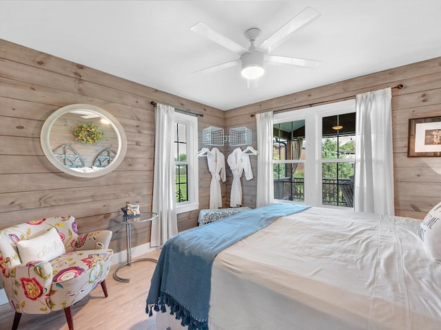 bedroom with multiple windows, ceiling fan, light wood-type flooring, and wooden walls