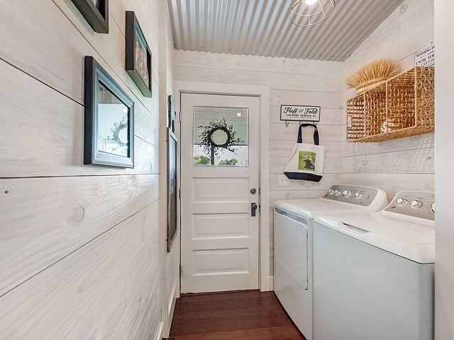 laundry room with dark wood-type flooring, wooden walls, and washer and dryer