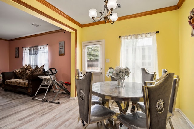 dining room featuring crown molding, light wood-type flooring, and an inviting chandelier