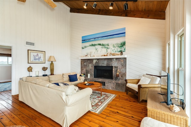 living room featuring track lighting, beam ceiling, hardwood / wood-style flooring, wood ceiling, and a fireplace