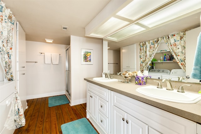 bathroom featuring double vanity, washing machine and dryer, hardwood / wood-style flooring, and a shower with shower door