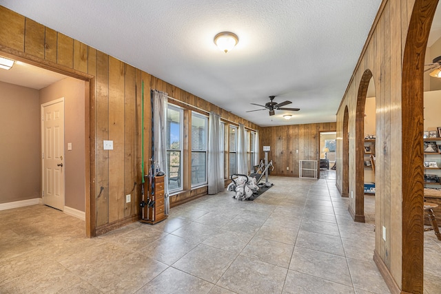 exercise room with arched walkways, wooden walls, a textured ceiling, and a ceiling fan