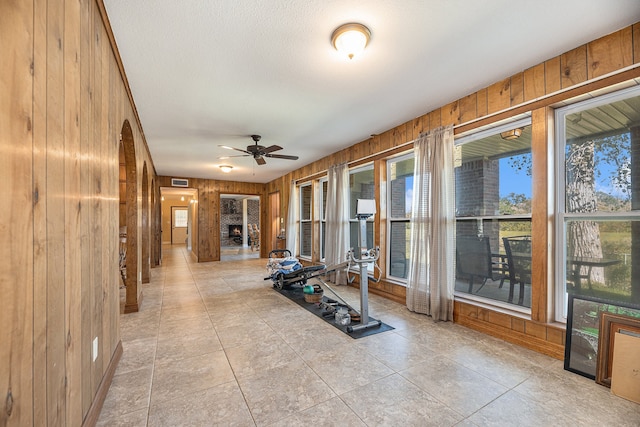 workout area featuring wooden walls, visible vents, arched walkways, ceiling fan, and a lit fireplace