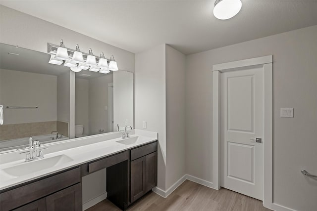 bathroom featuring toilet, wood-type flooring, a tub, and dual bowl vanity