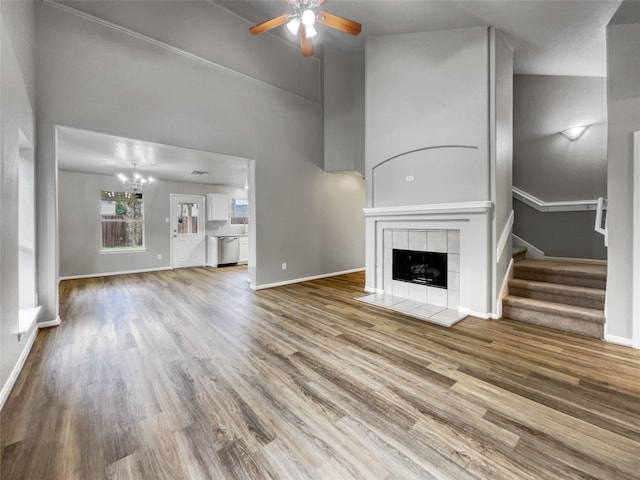 unfurnished living room featuring high vaulted ceiling, wood-type flooring, ceiling fan with notable chandelier, and a tile fireplace