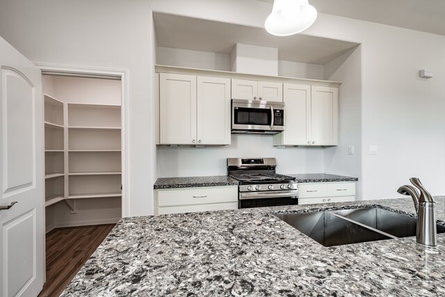 kitchen featuring appliances with stainless steel finishes, stone countertops, dark wood-type flooring, white cabinetry, and sink