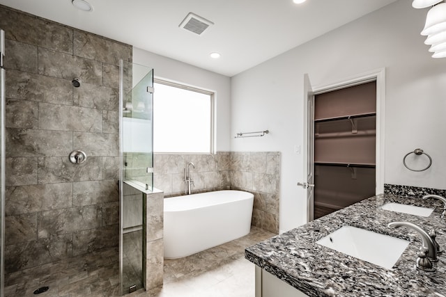 bathroom with tile flooring, double vanity, tile walls, and separate shower and tub