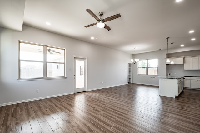 unfurnished living room featuring sink, ceiling fan with notable chandelier, and dark hardwood / wood-style floors