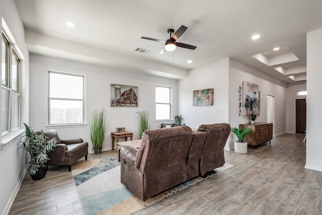 living room with ceiling fan, a tray ceiling, and light wood-type flooring