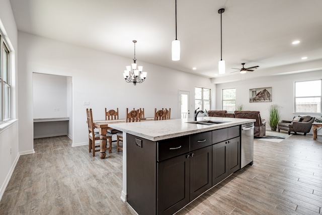 kitchen with dishwasher, ceiling fan with notable chandelier, a kitchen island with sink, sink, and light wood-type flooring