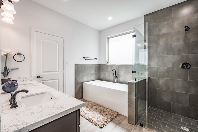 bathroom with tile walls, hardwood / wood-style floors, independent shower and bath, and dual vanity