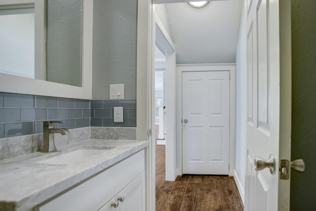 bathroom with vanity with extensive cabinet space, vaulted ceiling, backsplash, and hardwood / wood-style flooring