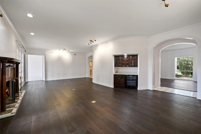 unfurnished living room with a tiled fireplace, wine cooler, crown molding, and dark hardwood / wood-style floors