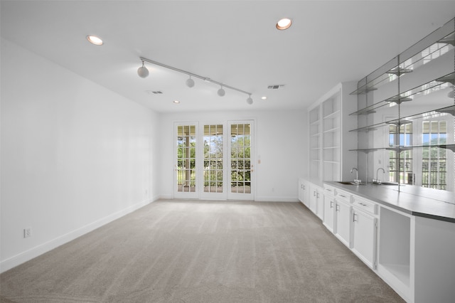 unfurnished living room with light colored carpet, sink, and track lighting