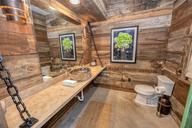 bathroom featuring concrete flooring, beam ceiling, toilet, and wood walls