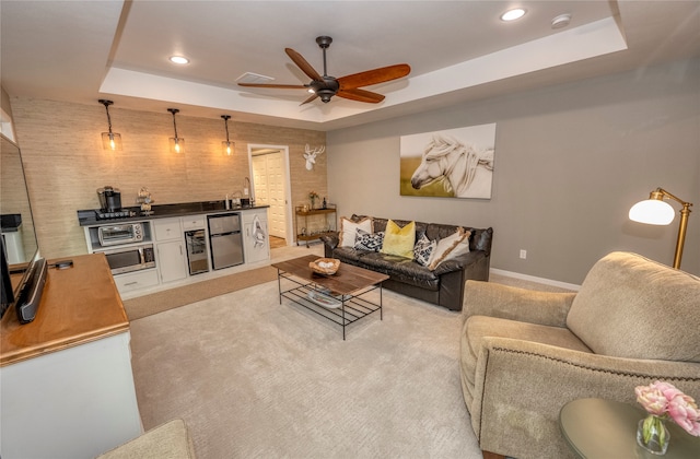 living room with ceiling fan, a raised ceiling, light colored carpet, and sink