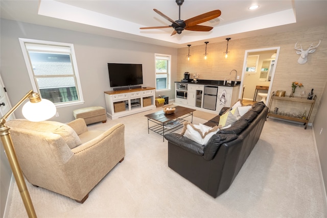 carpeted living room with a tray ceiling, bar, and ceiling fan