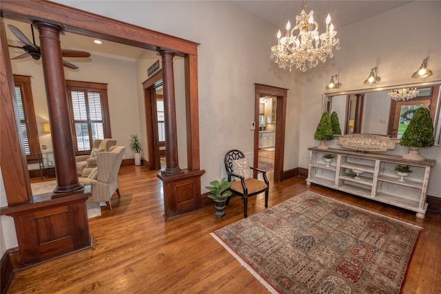 living area with ceiling fan with notable chandelier, wood-type flooring, and decorative columns