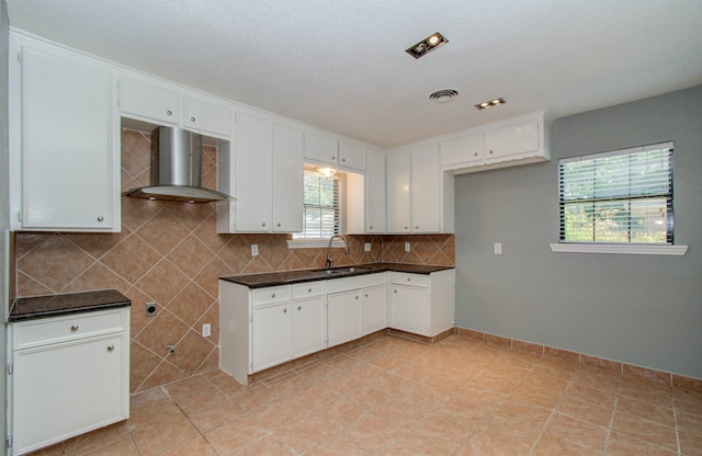 kitchen with tasteful backsplash, wall chimney exhaust hood, light tile floors, sink, and white cabinetry