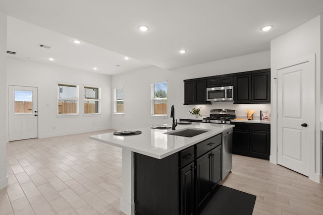 kitchen featuring sink, stainless steel appliances, a center island with sink, and light wood-type flooring