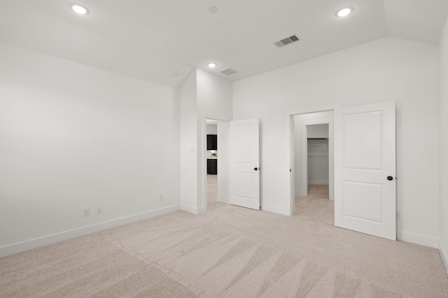 unfurnished bedroom featuring light colored carpet, a closet, vaulted ceiling, and a spacious closet