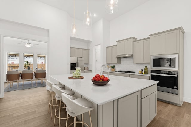 kitchen featuring gray cabinetry, appliances with stainless steel finishes, sink, light wood-type flooring, and a kitchen island with sink