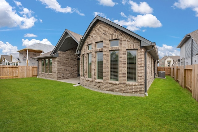 rear view of house with central AC unit and a lawn