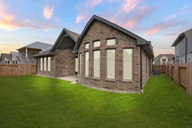 back house at dusk featuring a patio area, central AC, and a lawn